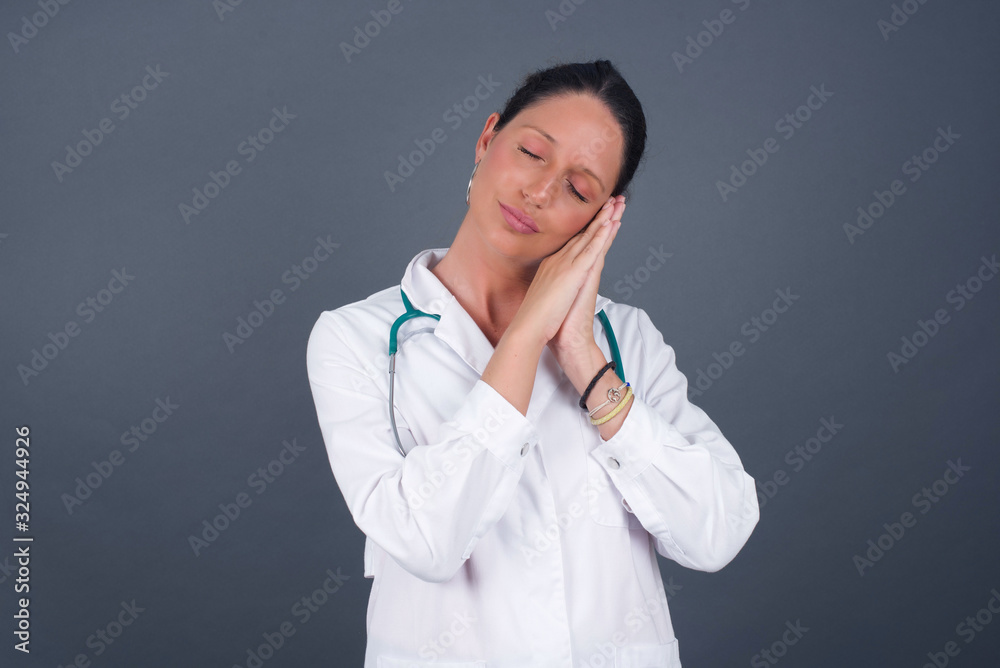 Relax and sleep time. Tired beautiful dark haired girl with closed eyes leaning on palms as pillow pretending sleeping being exhausted seeing dreams standing against gray background. Sleeping gesture. Relax and sleep time. Tired beautiful dark haired girl with closed eyes leaning on palms as pillow pretending sleeping being exhausted seeing dreams standing against gray background. Sleeping gesture.