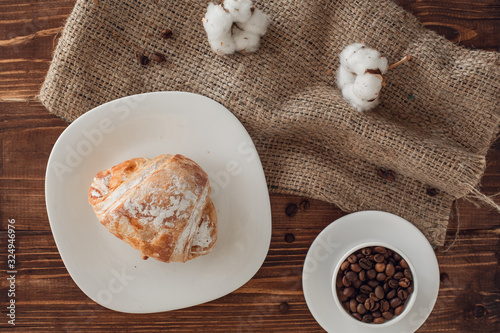 cup of coffee  croissant  burlap  coffee beans and cotton on brown wooden table