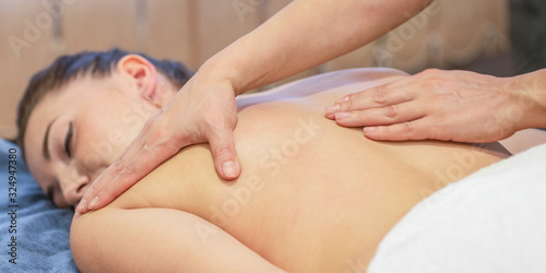 Hands of massage therapist are doing massage on back of young girl