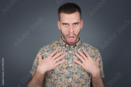 Shocked scared beautiful young man keeps hands on chest, mouth widely opened, stares at camera realizes that she forgot to pay bills, receives big fine, isolated outdoors. Girl saying: Who, me?