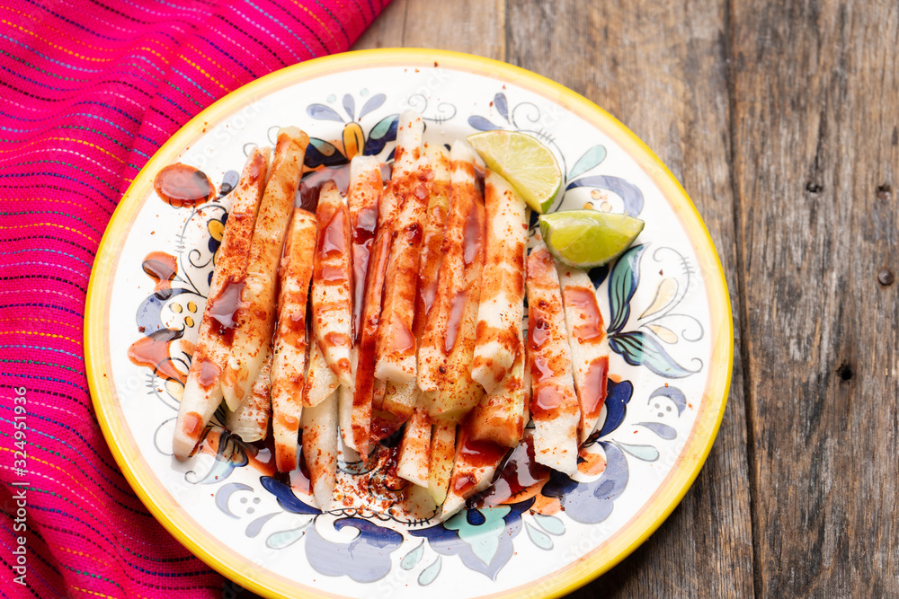 Mexican jicama cutted with chili powder and piquant sauce on wooden background Mexican jicama cutted with chili powder and piquant sauce on wooden background