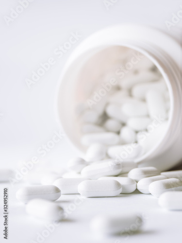 White pills spilled out of a plastic jar. Medicine capsules on white background.