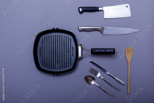 Metal knives with black on a grey table, grill pan, towel. Flat lay, layout with copy space.