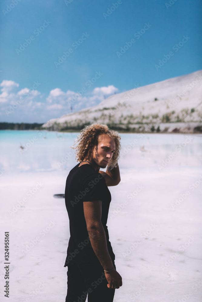 Curly blond man looking at the camera. Beach, clear water and blue sky. Tropical style. Travel.