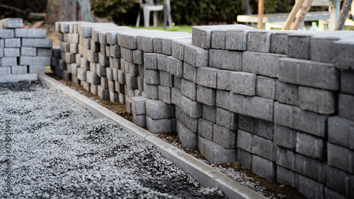 Laying gray concrete paving slabs along a house walkway. Stacks of concrete blocks are prepared to be layed on walk or patio on gravel foundation base.