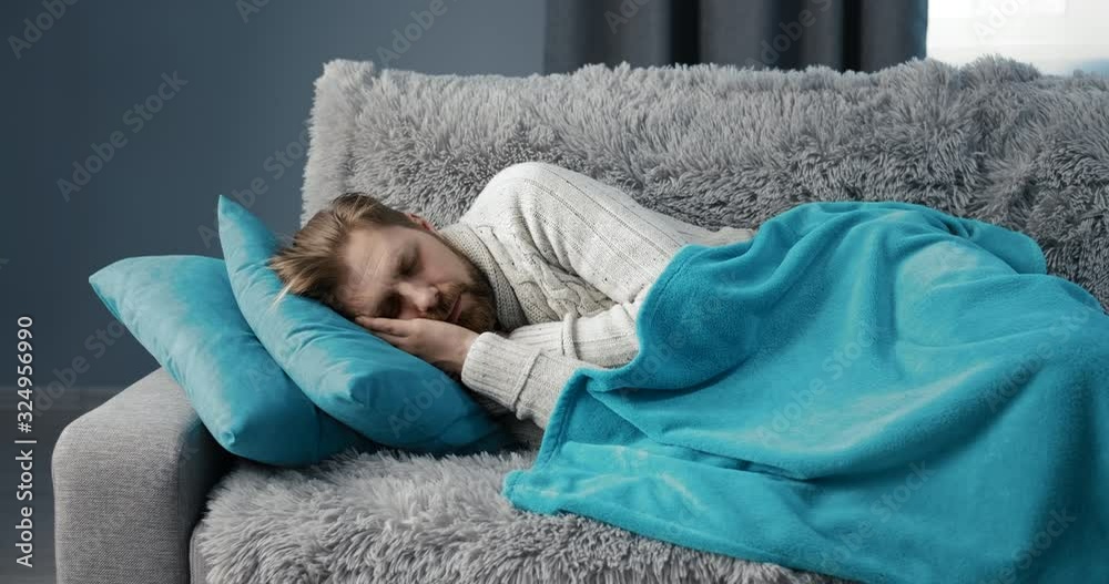 Coughing male covered with plaid sleeping on sofa, suffering influenza, epidemics