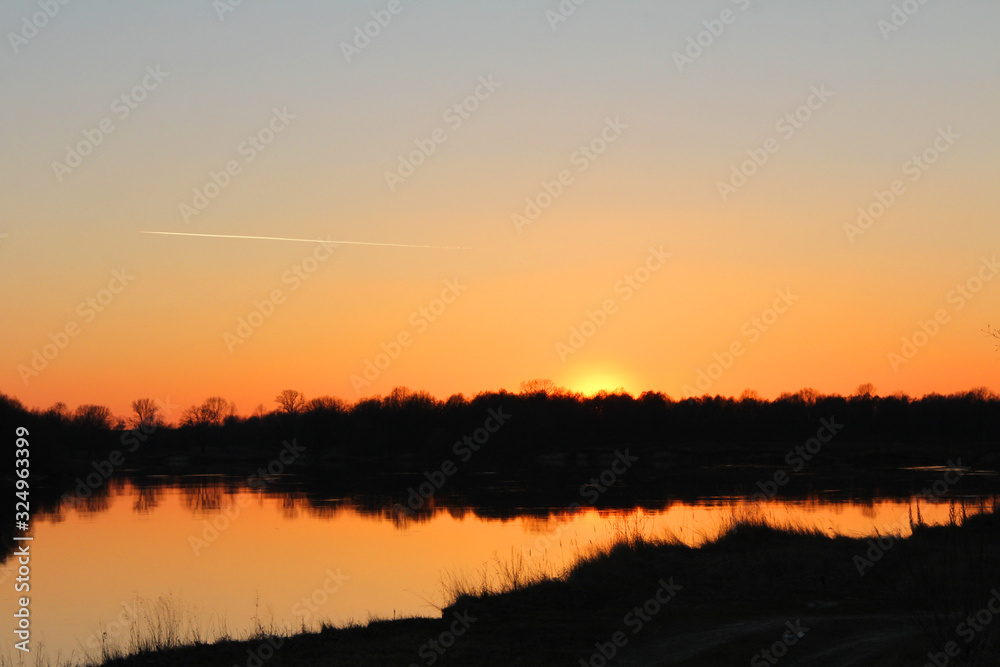 Fototapeta premium orange sunset behind the forest over the river in early spring