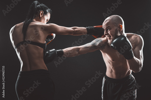 Shirtless Woman exercising with trainer at boxing and self defense lesson, studio, dark background. Female and male fight. © zamuruev