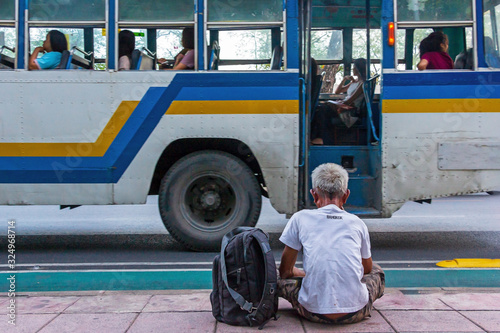 An old man sit near the road with a bus in Bangkok Thailand.