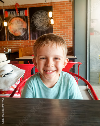 Portrait of happy smiling toddler boy sitting in cafe and looking in camera photo