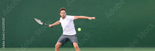 Tennis player man header banner hitting ball with racket on green horizontal copy space background. Sports athlete training forehand grip technique on outdoor court. © Maridav