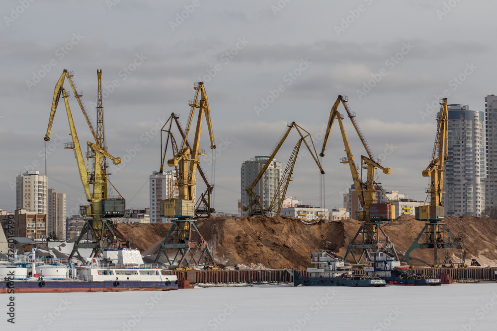 River cargo port in Moscow, Russia. Cargo ship being loaded up by a crane for loading bulk materials at port of Moscow, Russia. yellow cargo cranes in the river port. 