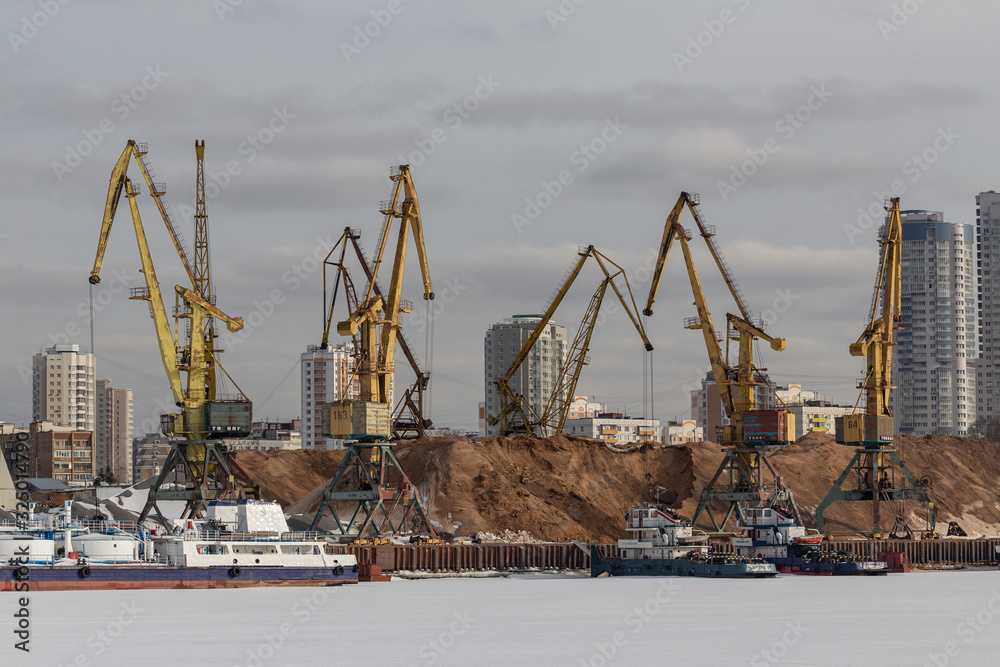 River cargo port in Moscow, Russia. Cargo ship being loaded up by a crane for loading bulk materials at port of Moscow, Russia. yellow cargo cranes in the river port. River cargo port in Moscow, Russia. Cargo ship being loaded up by a crane for loading bulk materials at port of Moscow, Russia. yellow cargo cranes in the river port.
