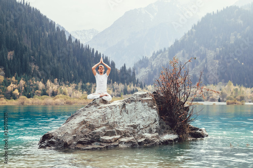 Caucasian yoga man in outdoor meditation sitting on lonely rock island of mountain lake. photo