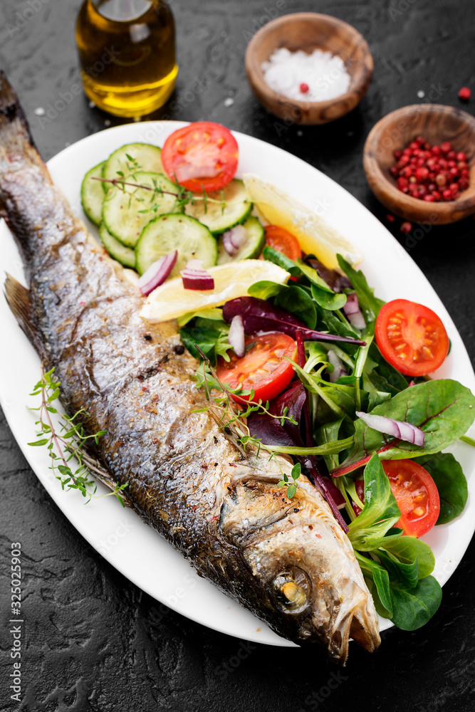 White plate of baked sea bass with fresh green salad. White plate of baked sea bass with fresh green salad.