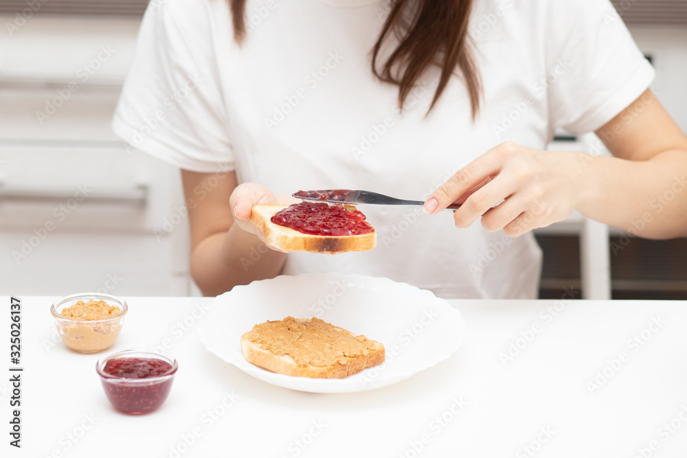 Female hands spread raspberry jam on bread, prepare sandwiches in the morning at home for breakfast for the whole family