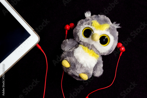 Owl toy lying with red earphones, listenning to music via earphones