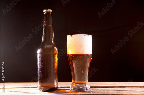 Cold tasty beer on a hot summer day. Bottle and glass of beer on a wooden table against black background and copy space