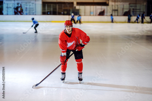 Full length of attractive hockey player skating on the ice towards camera with stick in his hands.