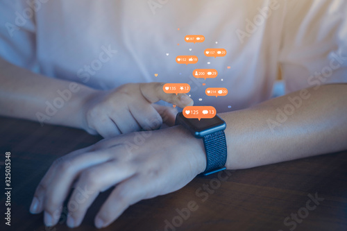 Person using a social media marketing concept on smartwatch with notification icons of like, message, comment and star above smartwatch screen.