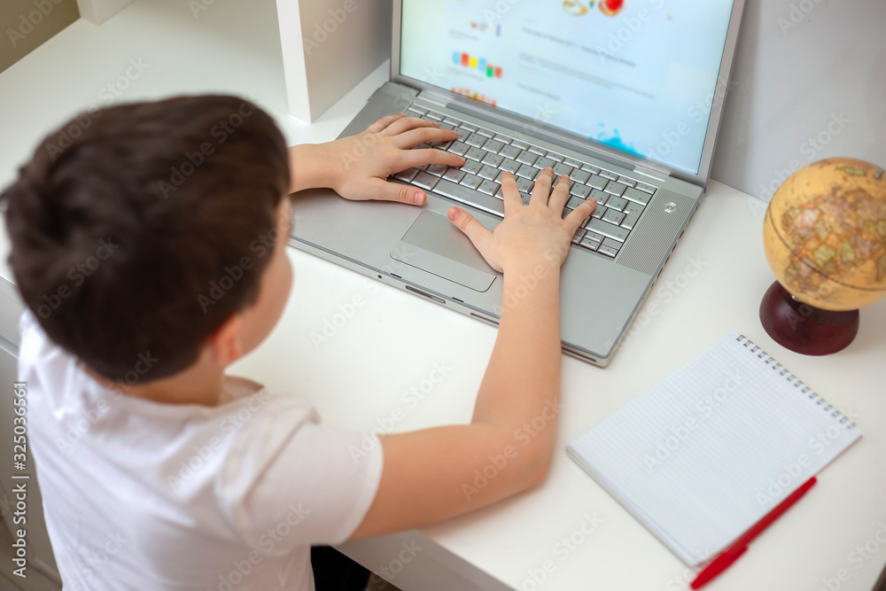 The boy sits with his back behind a laptop, fingers on the keyboard The boy sits with his back behind a laptop, fingers on the keyboard