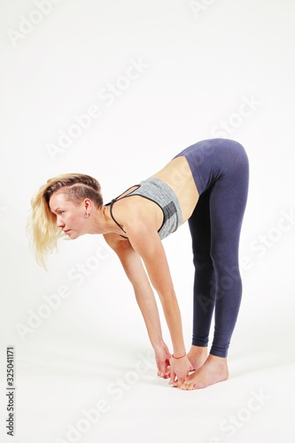Young woman practicing yoga,standing in an exercise leaning forward to straight legs, holding hands, toes, padangushthasana pose, balance workout,sportswear, pants, bra, short,studio,white background