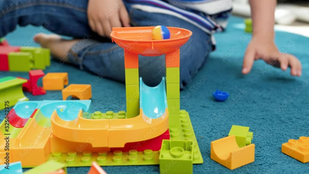 4k closeup video of colorful ball rolling in toy marble run built by little toddler boy