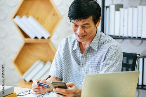 The aged Asian businessman holds a credit card to view online spending.