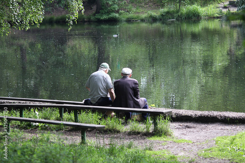 Two elderly men on a bench near a pond. People