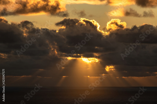 Long aerial view of sun cast its golden rays down upon sea surface through dark dramatic clouds