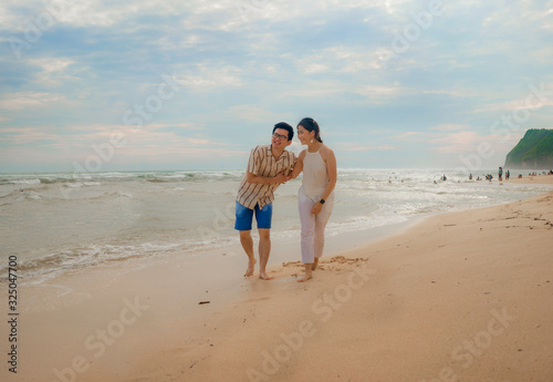 romantic lifestyle portrait of young Asian Korean couple in love enjoying holiday on beautiful beach walking together by the sea playful and carefree  in happy relationship