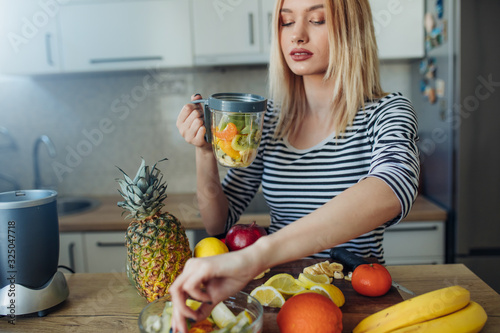 Young woman preparing smoothie. Young woman preparing healthy fruit drink at the kitchen.