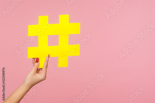 Closeup of hand holding large yellow paper hashtag symbol next to copy space, hash sign of famous media content, social media marketing and blog promotion. studio shot isolated on pink background photo