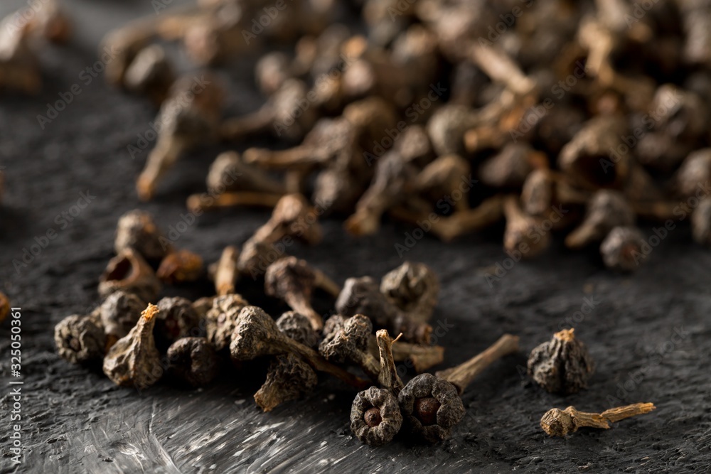 Heap of raw, dried cinnamon blossom buds spice on rustic black table background Heap of raw, dried cinnamon blossom buds spice on rustic black table background