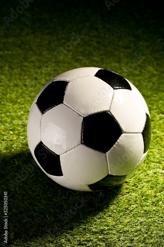 Single soccer ball on green grass lawn background with harsh stadium lighting
