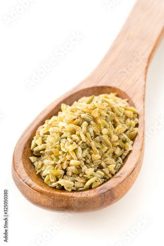 Heap of uncooked, raw freekeh or firik, roasted wheat grain, in wooden spoon over white