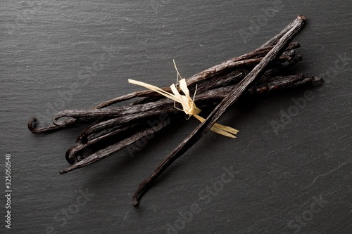 Bundle of tied, dried bourbon vanilla beans or pods on black stone board flat lay top view photo