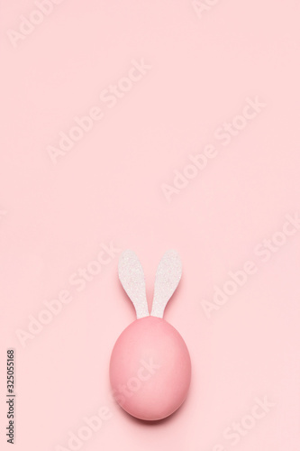 Huevo de pascua de color rosa pastel con orejas de conejo de color blanco sobre fondo rosa pastel vertical. photo