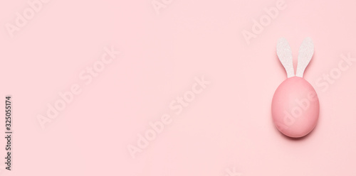 Huevo de pascua de color rosa pastel con orejas de conejo de color blanco sobre fondo rosa pastel horizontal.
