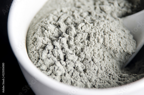 Gray bentonite clay powder in a bowl. Diy facial mask and body wrap recipe. Natural beauty treatment and spa. Clay texture close up. Selective focus.