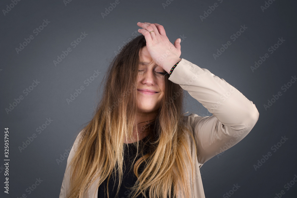 Exasperate female keeps hands on temples, feels strong headache, closes eyes with pain, need healthy sleep, being overworked, fatigue and tired. Europea woman being ill, isolated over gray background Exasperate female keeps hands on temples, feels strong headache, closes eyes with pain, need healthy sleep, being overworked, fatigue and tired. Europea woman being ill, isolated over gray background