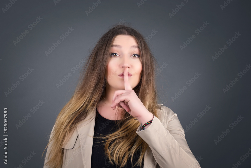 Dont tell my secret or not speak too loud, please! Emotional surprised student makes hush gesture, asks be quiet, has scared expression as afraids of revealing secret, poses against gray studio wall. Dont tell my secret or not speak too loud, please! Emotional surprised student makes hush gesture, asks be quiet, has scared expression as afraids of revealing secret, poses against gray studio wall.