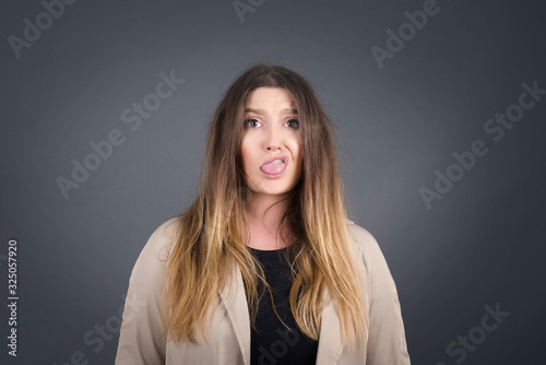 Body language. Disgusted stressed out pretty girl with straight fair hair posing against gray wall, frowning her face, demonstrating aversion to something.