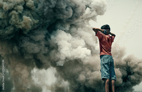 Homeless little boy watching bombarded city between smoke.