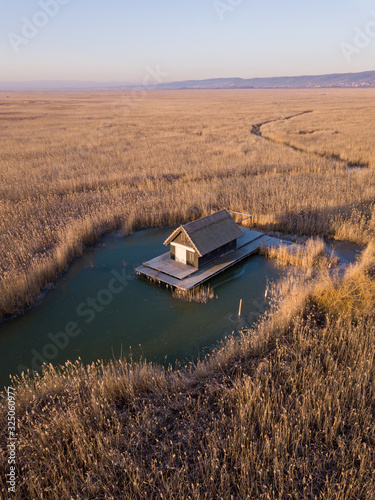 A small hut in a reed field in the middle of the Schilfgürtel of Neusiedler See near Breitenbrunn in Burgenland Austria on a cold winter morning with frozen water
