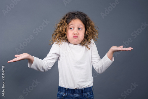 Puzzled and clueless little girl with arms out, shrugging her shoulders, saying: who cares, so what, I don't know. Negative human emotions, facial expressions, life perception and attitude.