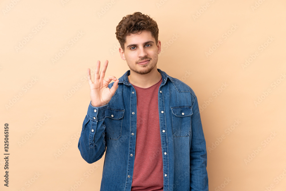Caucasian man isolated on beige background showing an ok sign with fingers Caucasian man isolated on beige background showing an ok sign with fingers