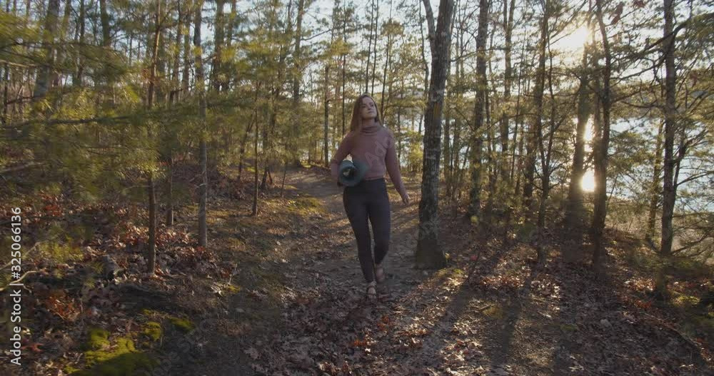 A woman walks through the woods holding a yoga mat A woman walks through the woods holding a yoga mat