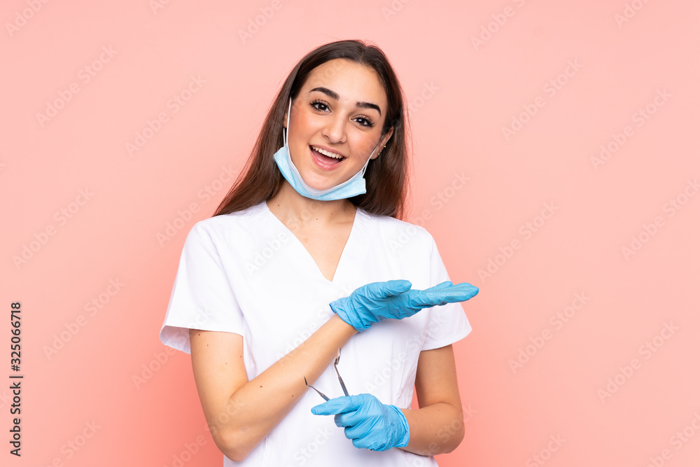 Woman dentist holding tools isolated on pink background extending hands to the side for inviting to come Woman dentist holding tools isolated on pink background extending hands to the side for inviting to come