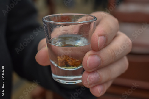 Closeup of male hand holding vodka glass with vodka and plum inside